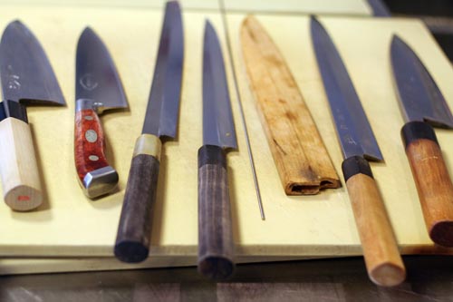 Part of Suzuki's knife kit. 2 debas, 2 yanagis, the needle, a saya cover, and another yanagi and deba.